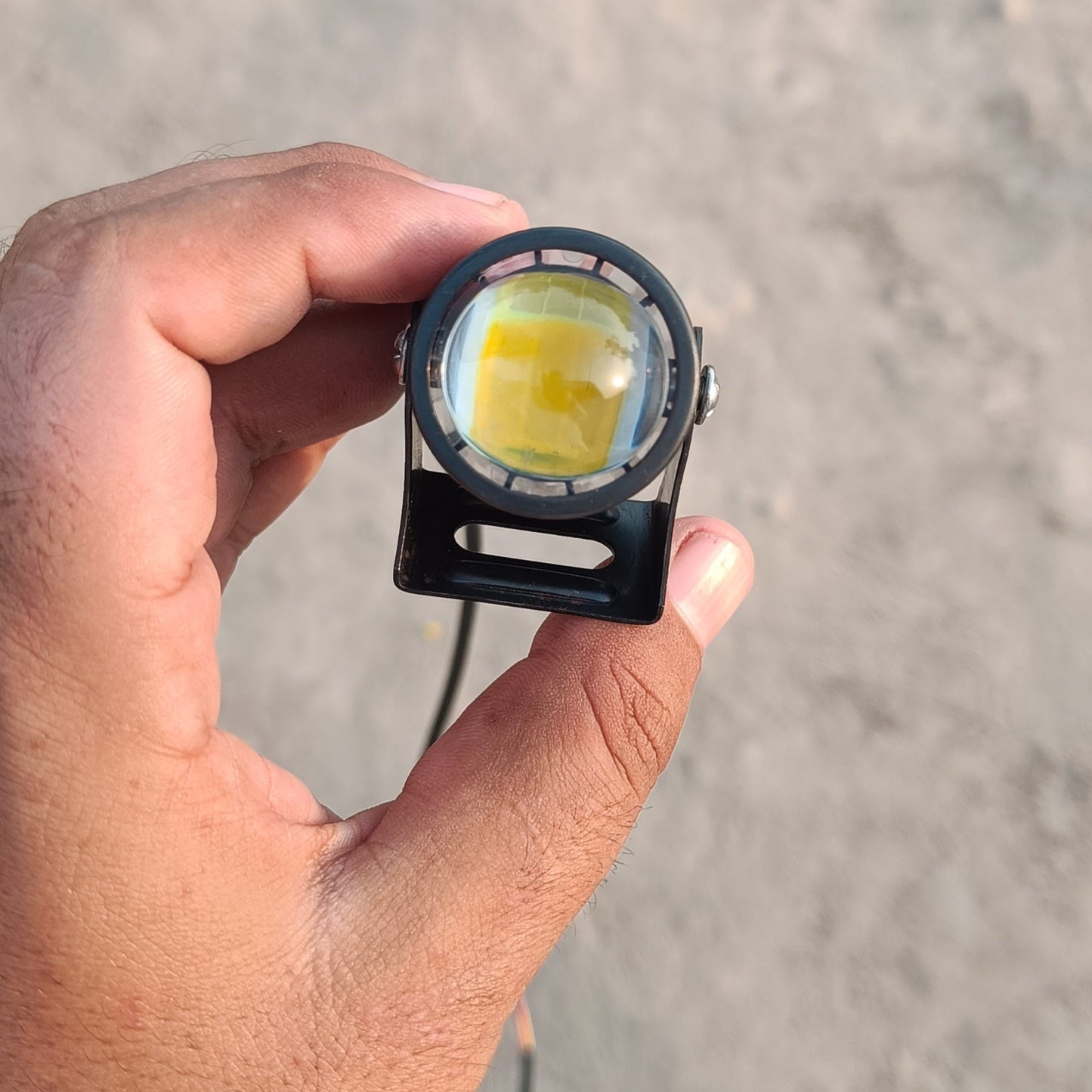 Hand holding a small round device with a yellow light on a sandy background