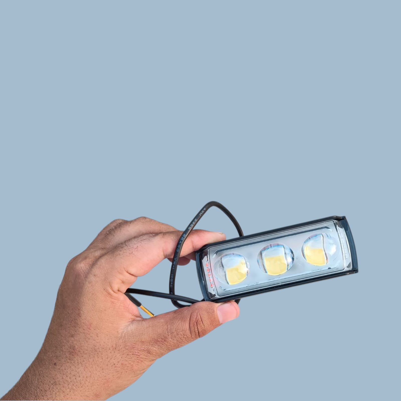 Hand holding a small rectangular light fixture with three visible LEDs against a gray background