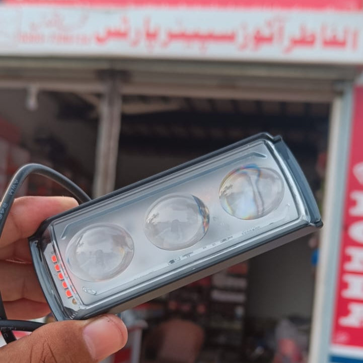Hand holding a car light bulb in front of a store with Arabic text