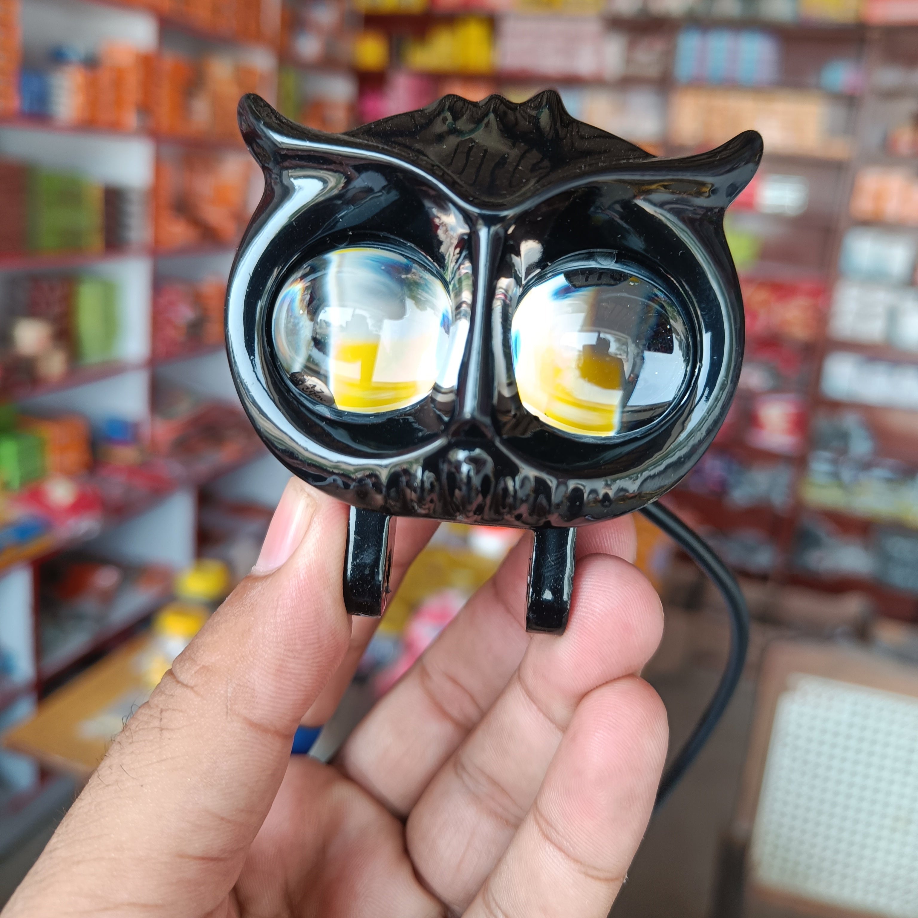Black owl-shaped light held in front of a store shelf with various products.